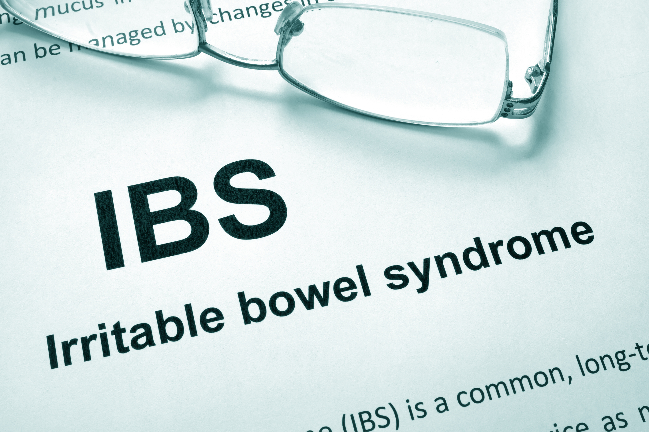 White paper with words Irritable bowel syndrome IBS. Gray glasses sit on top of the paper.